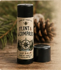 Flint & Compass lip balm tube with its cap, beside a pine cone and pine needles